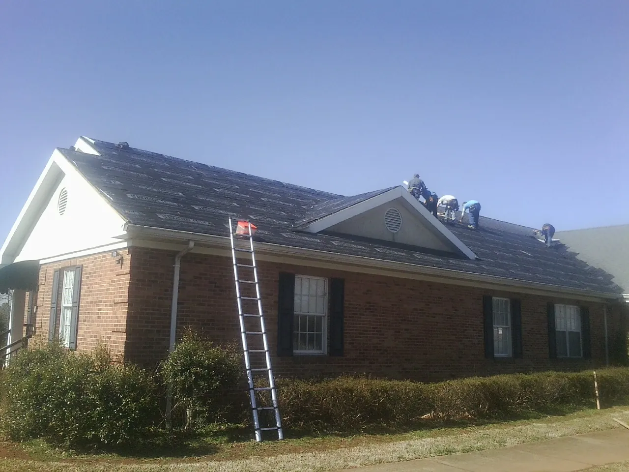 Crew tearing shingles off a brick ranch roof with a ladder set — Metal Roof Repair work by our crew in Warwick