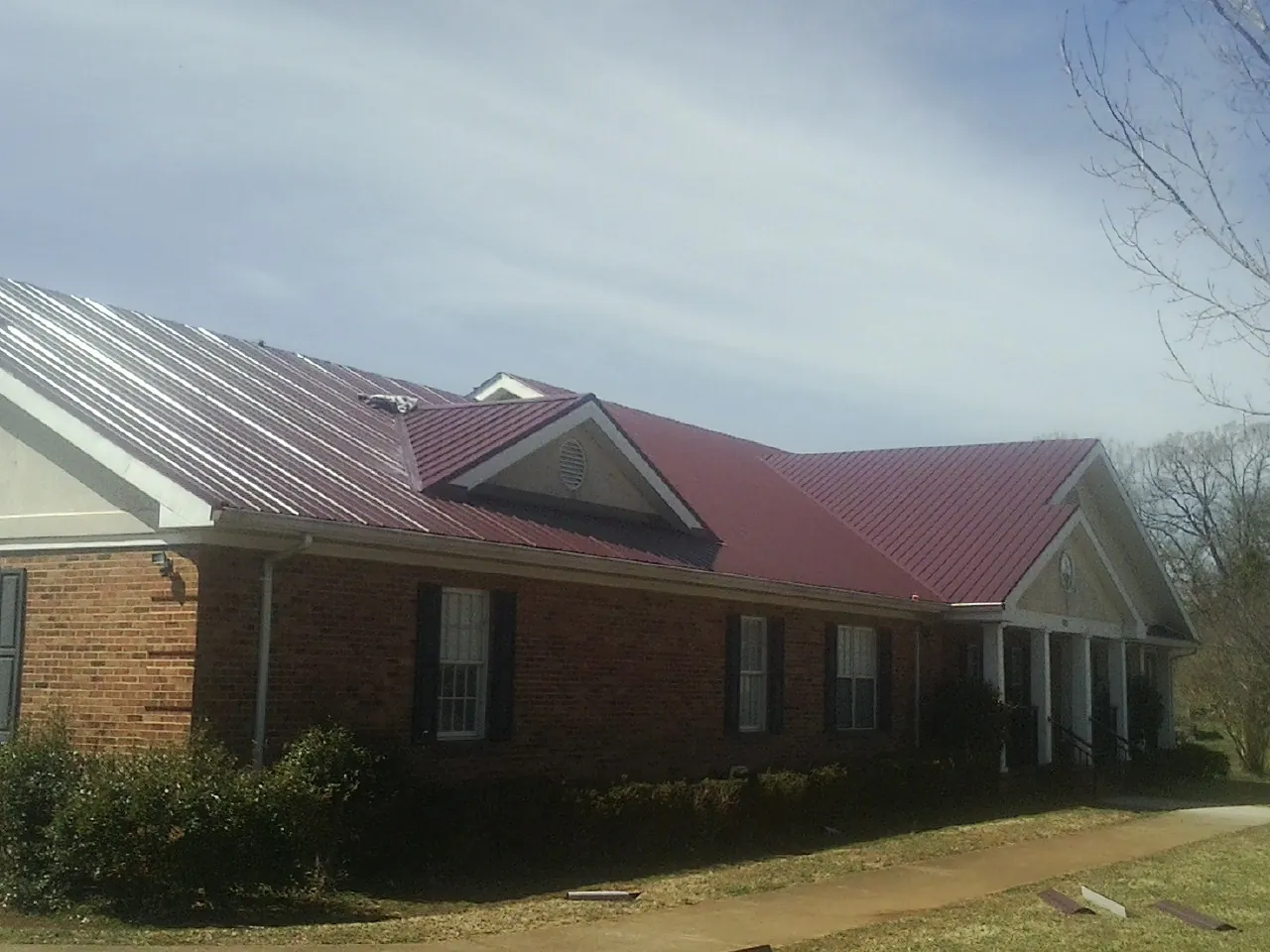 Red metal roof with gabled entries on a long brick building, from a Hail Damage Roof Repair job in Warwick
